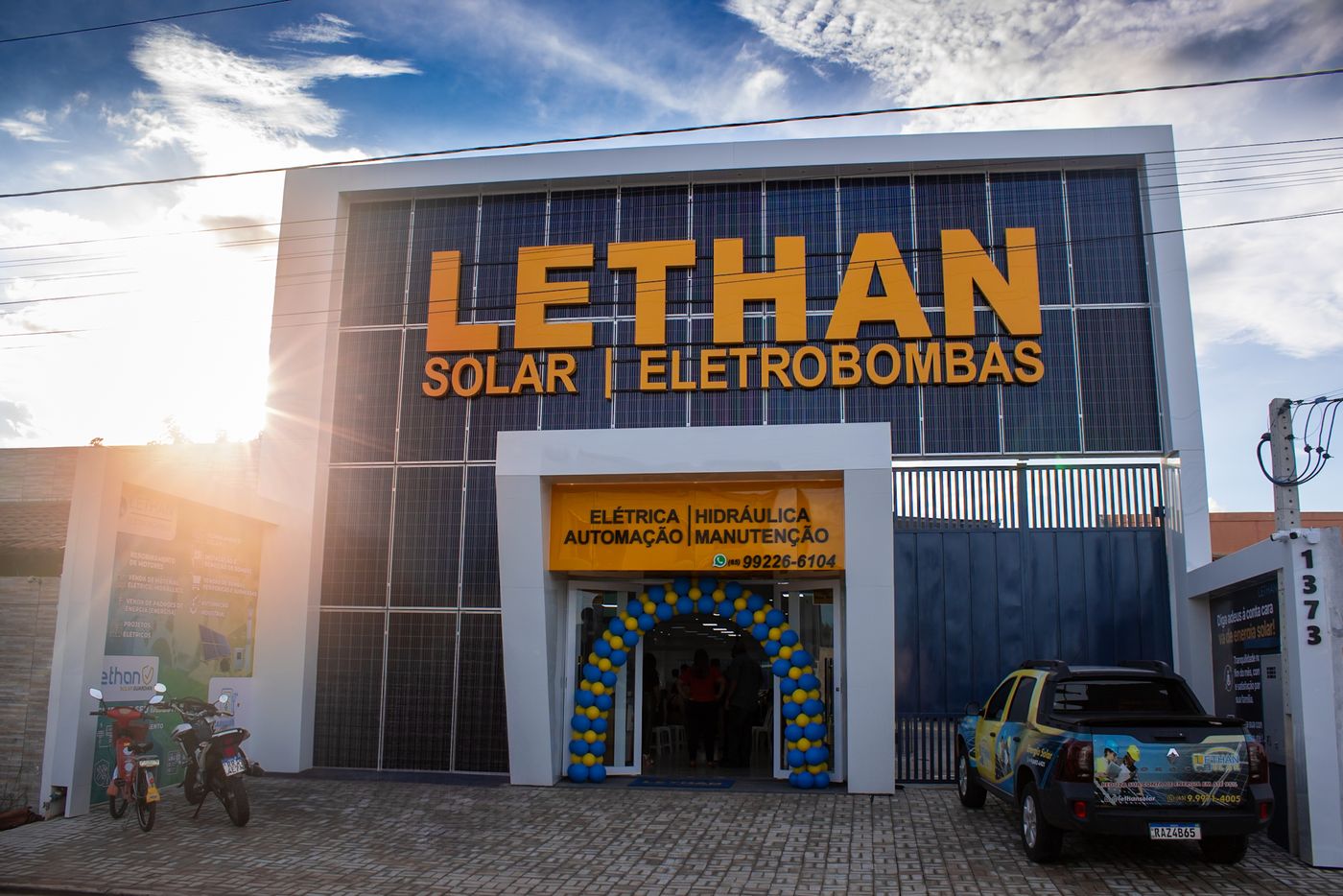 Fachada da sede do Grupo Lethan em Cáceres-MT, com placas solares cobrindo o prédio, marca LETHAN em letreiro amarelo e caminhonete personalizada na frente